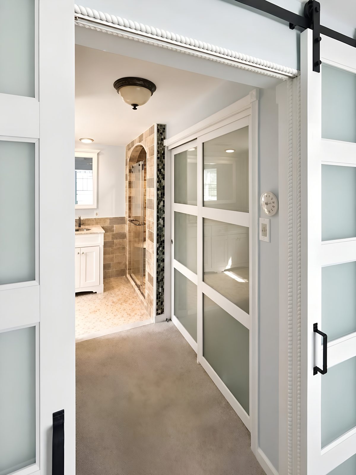 Frosted sliding barn doors leading into the remodeled bathroom, with the arched shower visible beyond