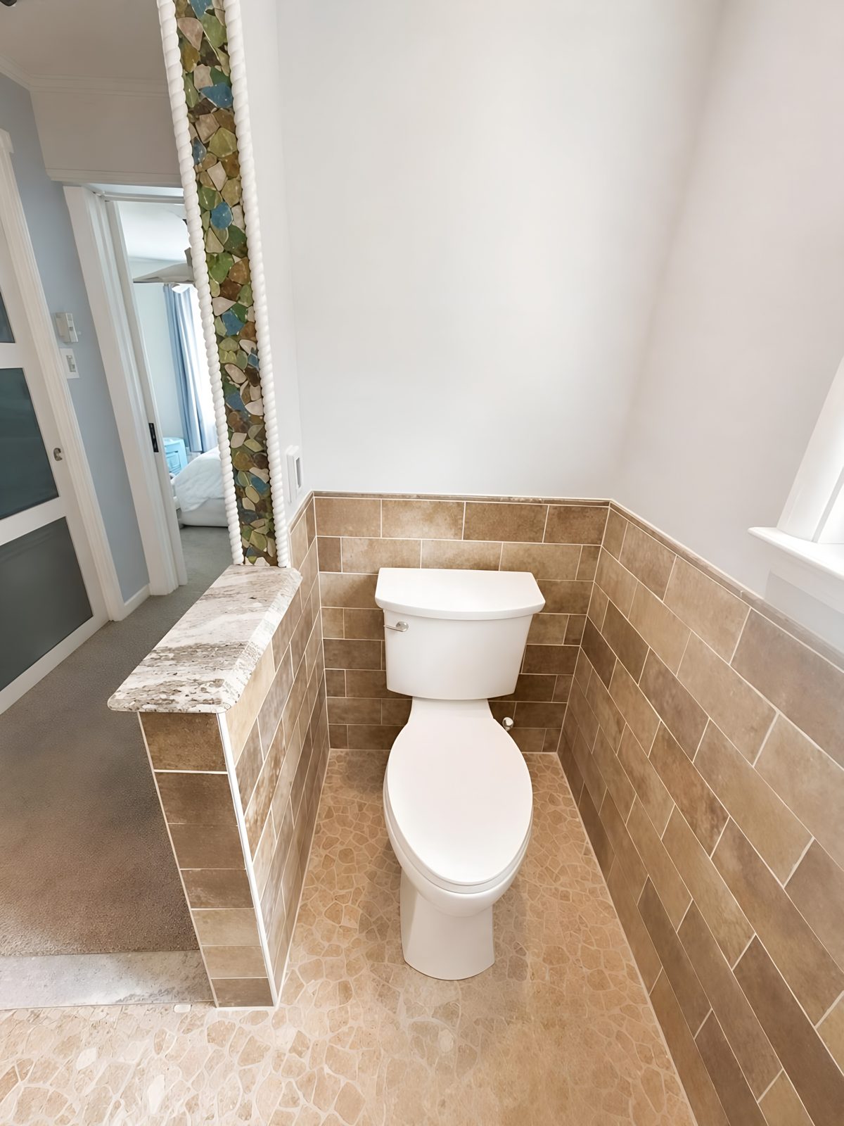 New toilet against a tiled half-wall with a stone cap and heated tile floor