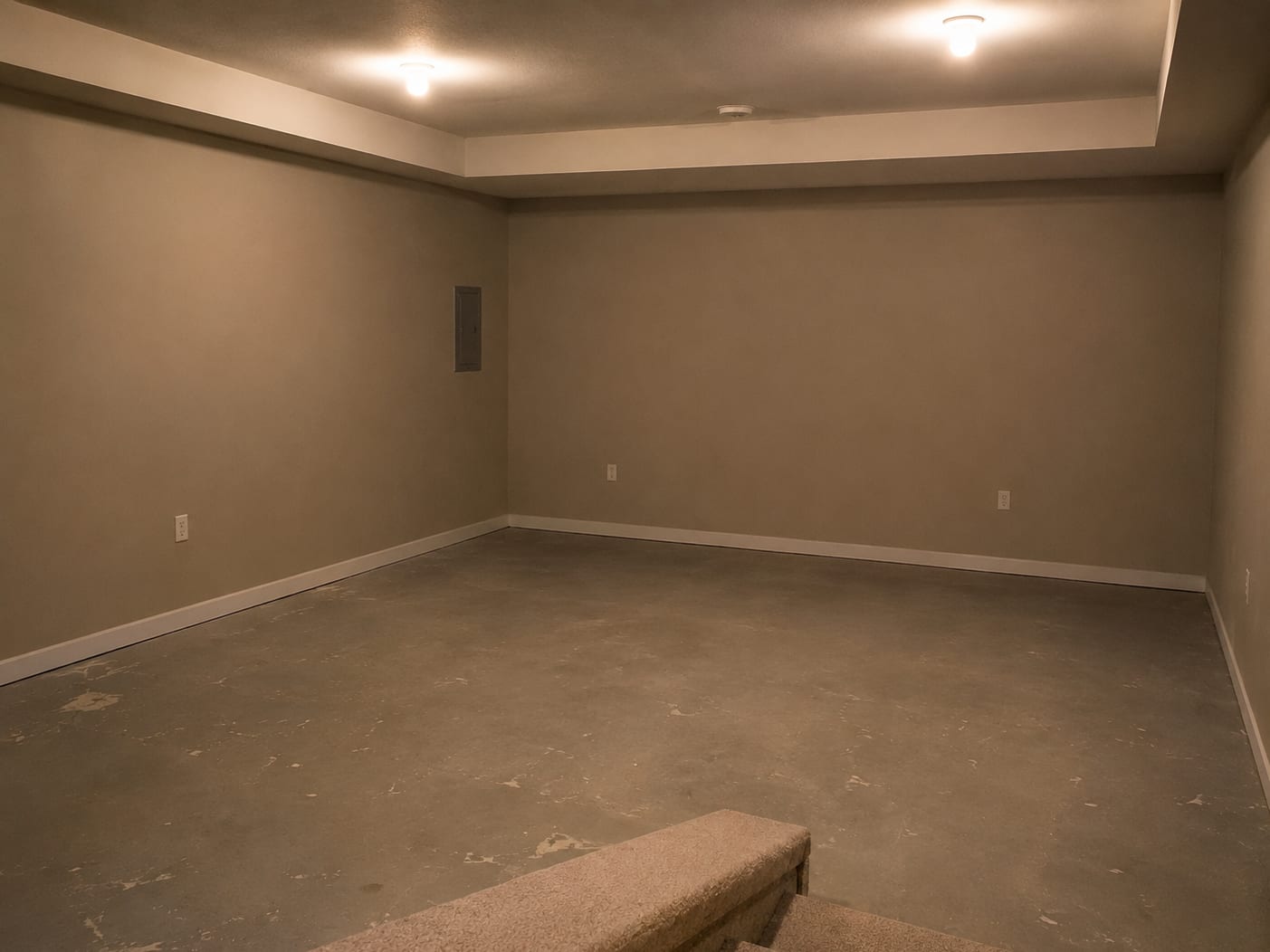 Bare unfinished basement with beige walls, concrete floor, tray ceiling, and an electrical panel